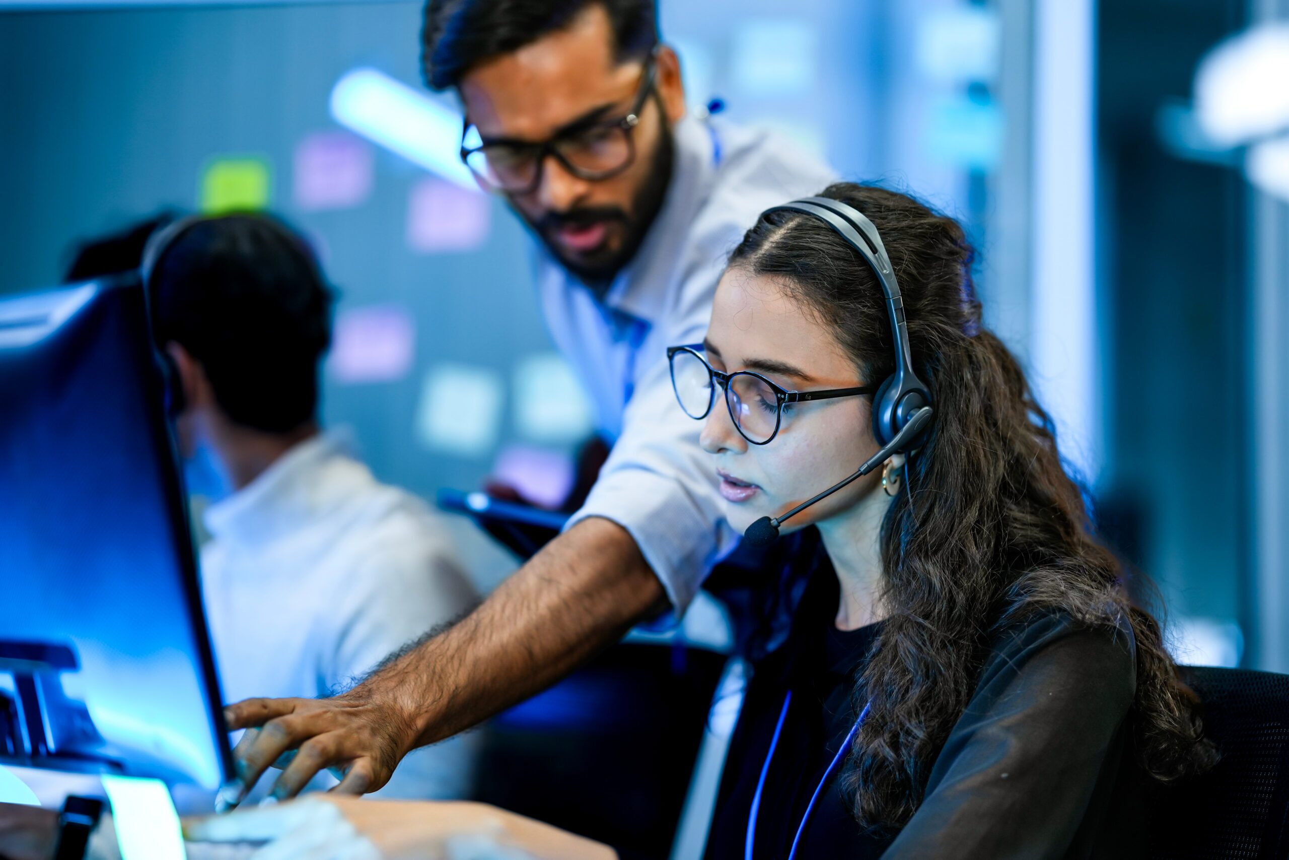 man pointing at screen with woman looking at screen and with a headset on
